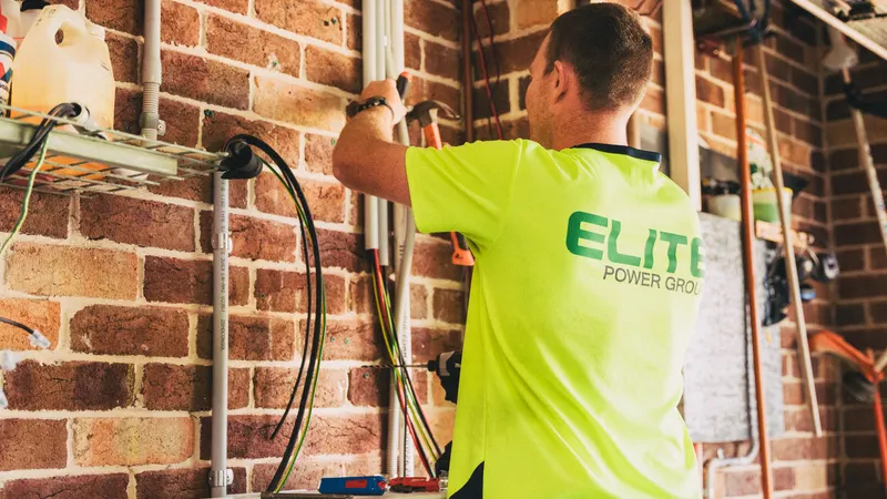 Električar radi na vodičima i instalacijskim cijevima na zidu od opeke